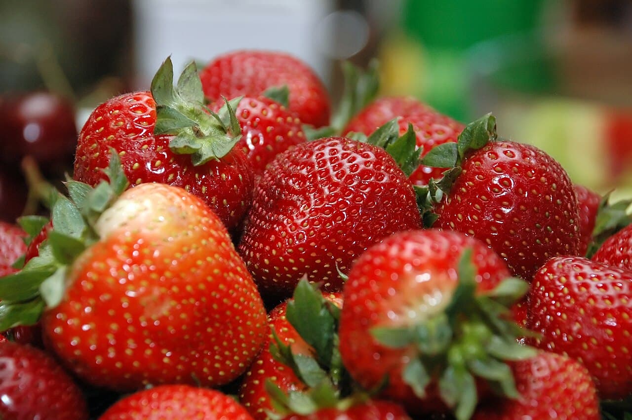 A close-up heap of ripe red strawberries with green leafy caps, glossy and freshly picked
